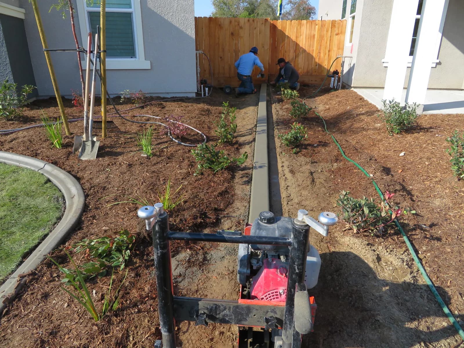 The crew trenching irrigation lines along a new planting bed beside a house