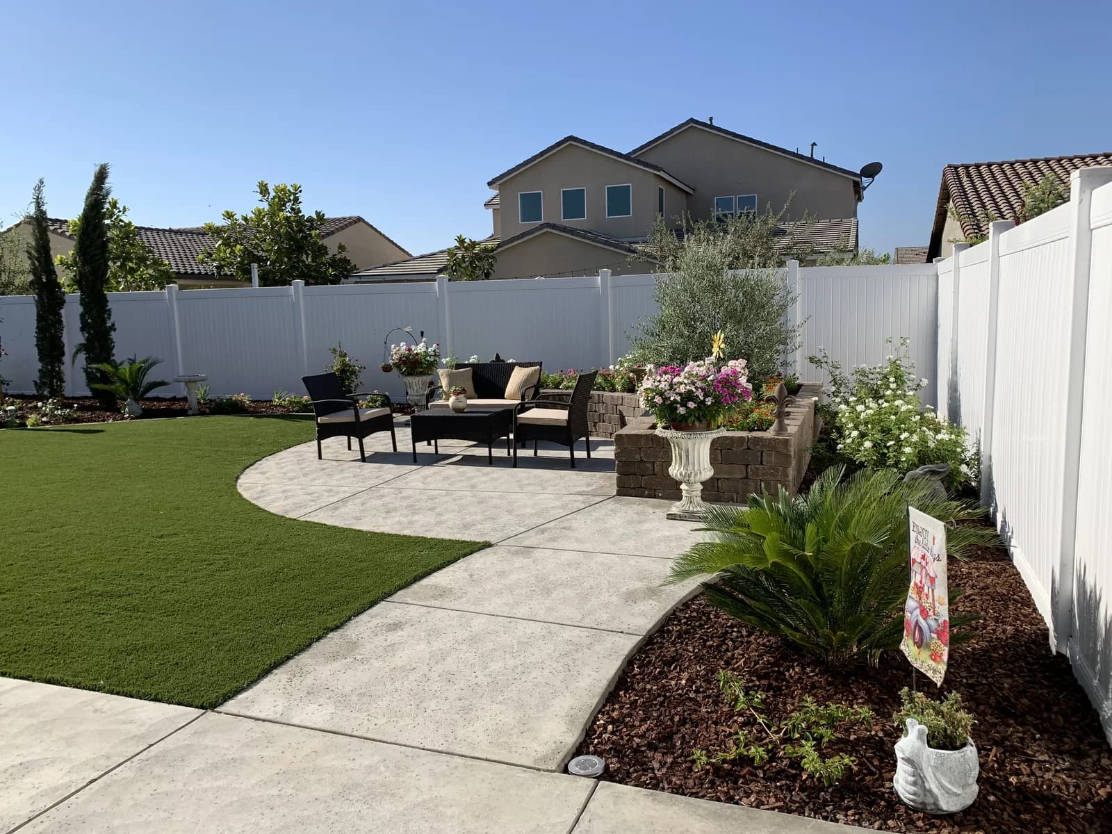 A curved concrete patio with a seating area and planters, set in artificial grass