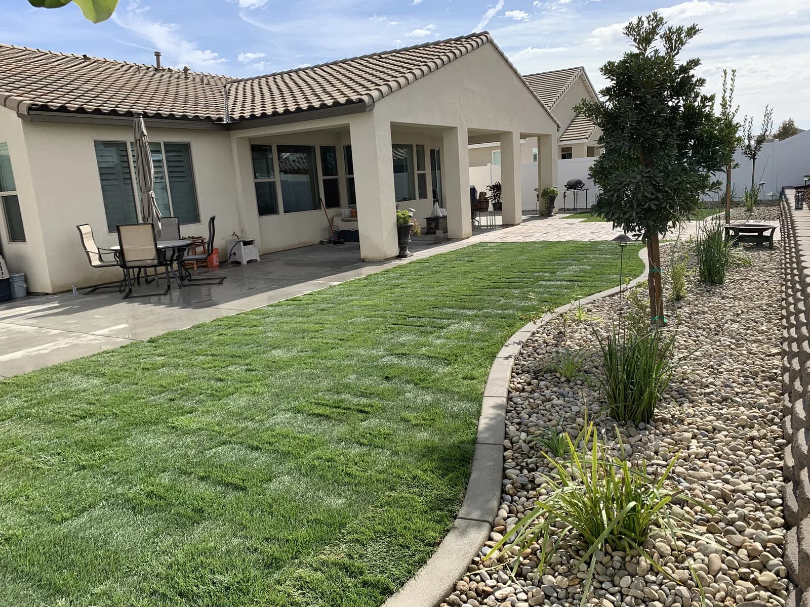 Concrete walkway curving between a lawn and a bed of river rock, with a covered patio behind