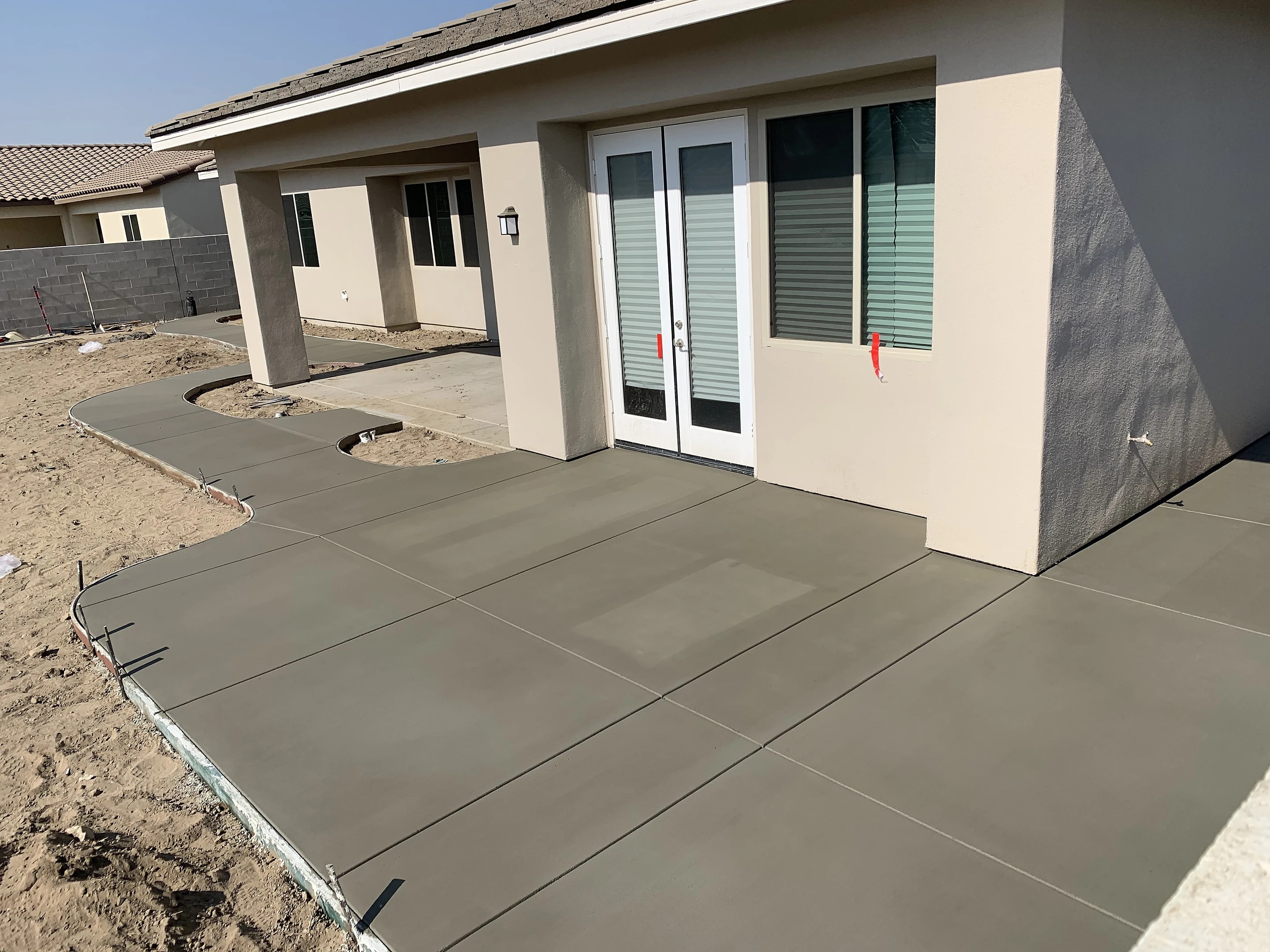 New concrete patio poured behind a newly built home, the yard still bare dirt