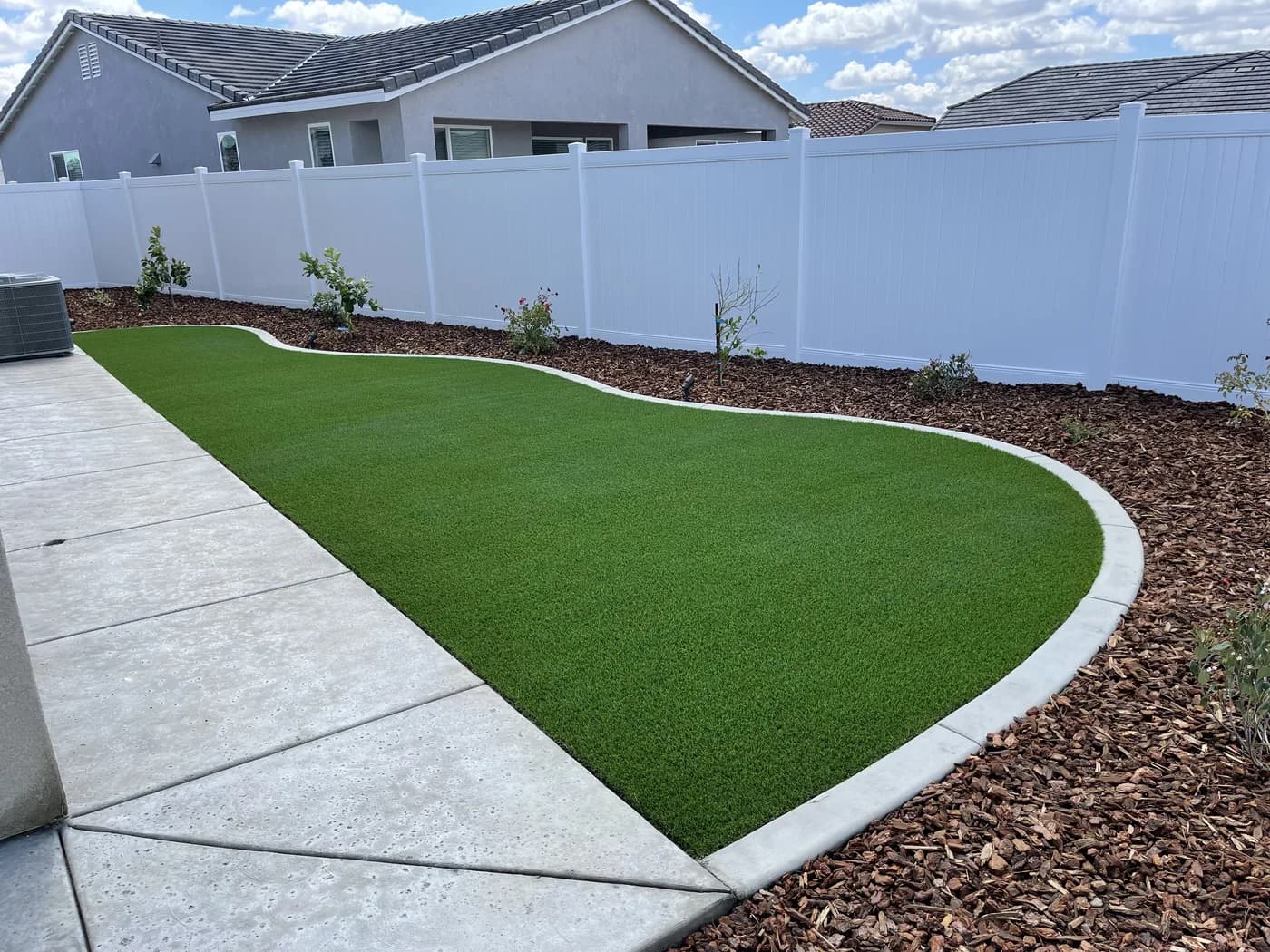 Concrete walkway running beside an artificial turf lawn edged with a concrete curb