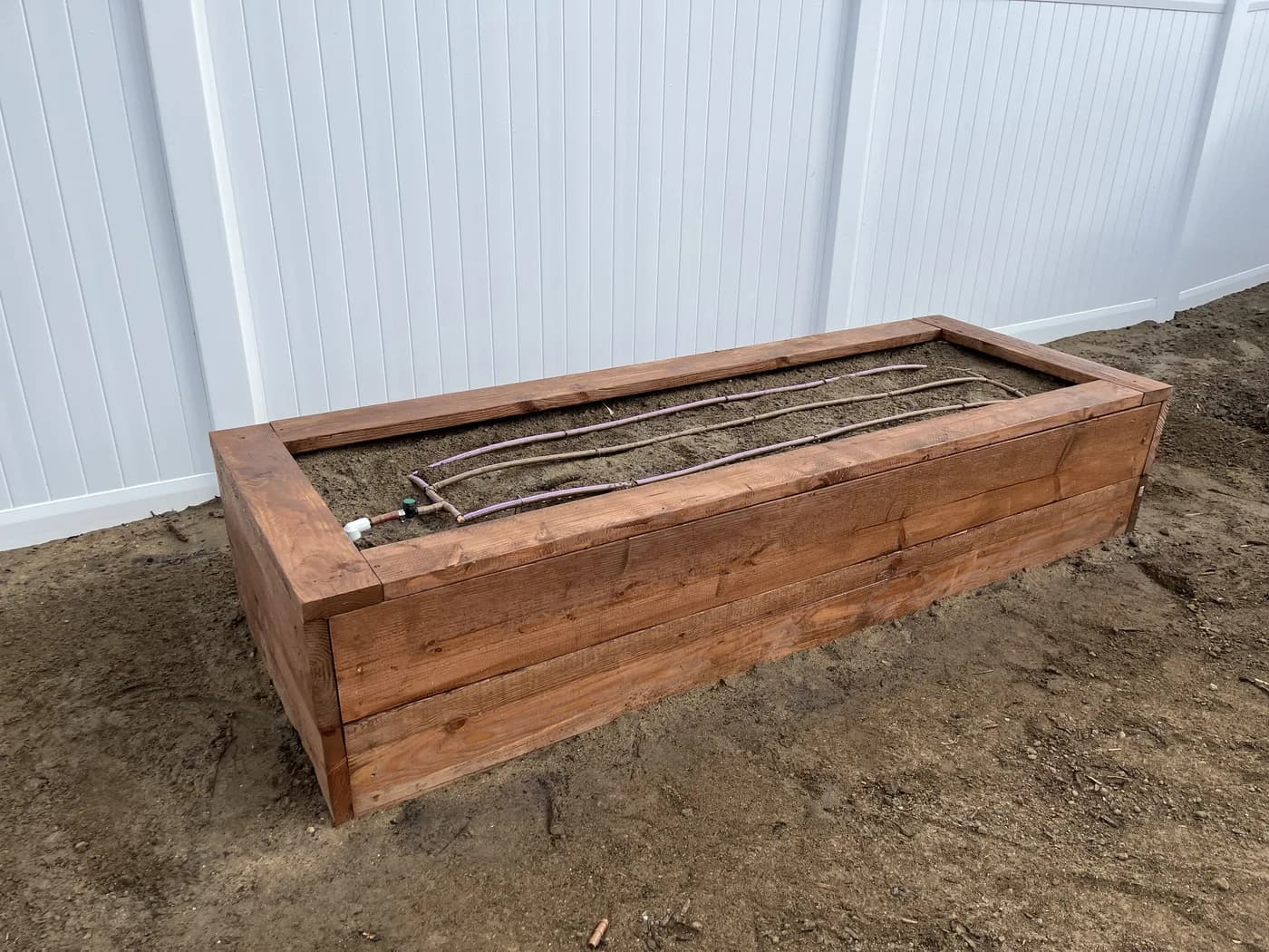 Drip lines laid in a wooden planter box beside a white fence