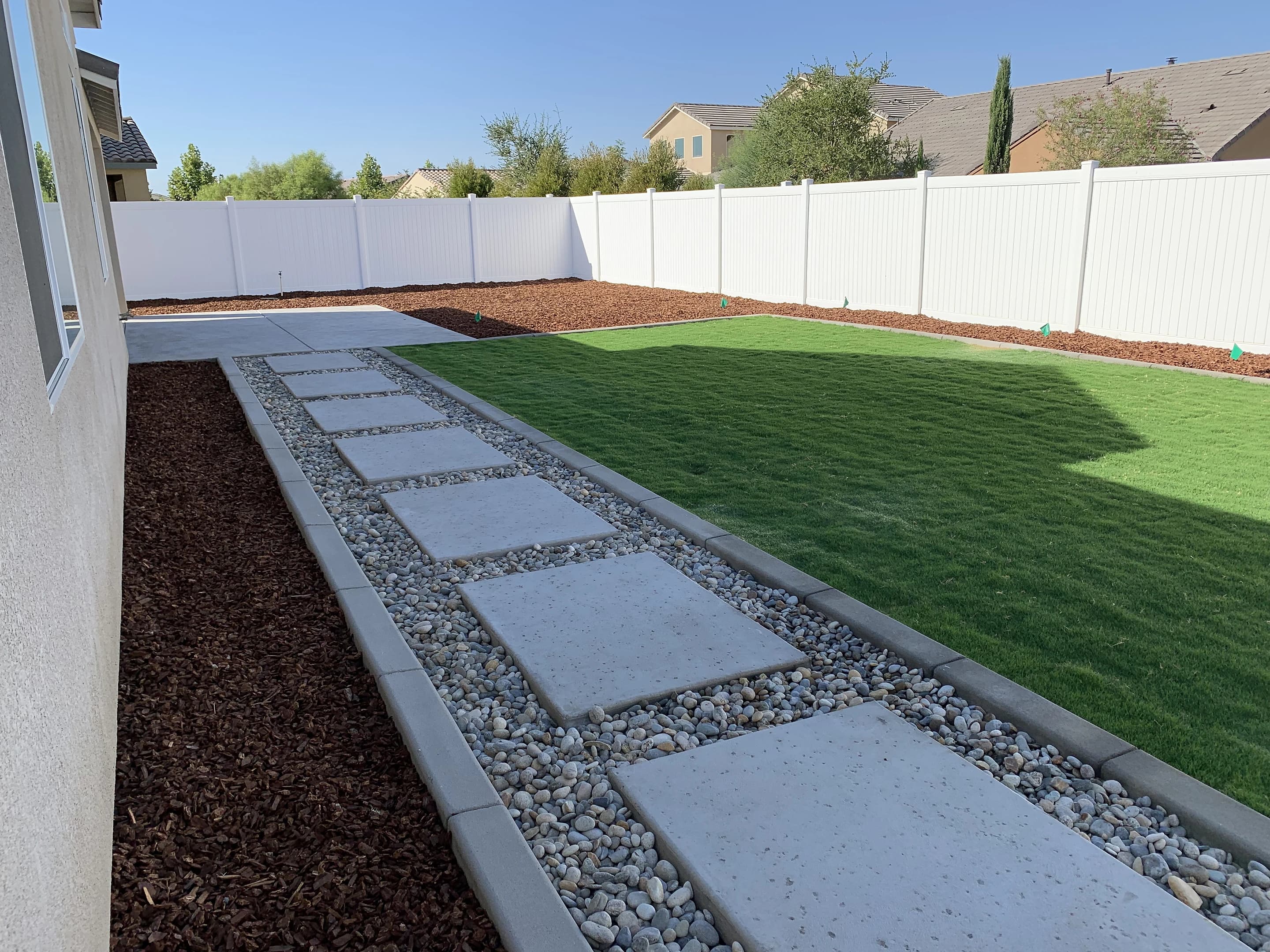 Concrete stepping pads set in river rock along a new lawn, with a bark bed on the other side