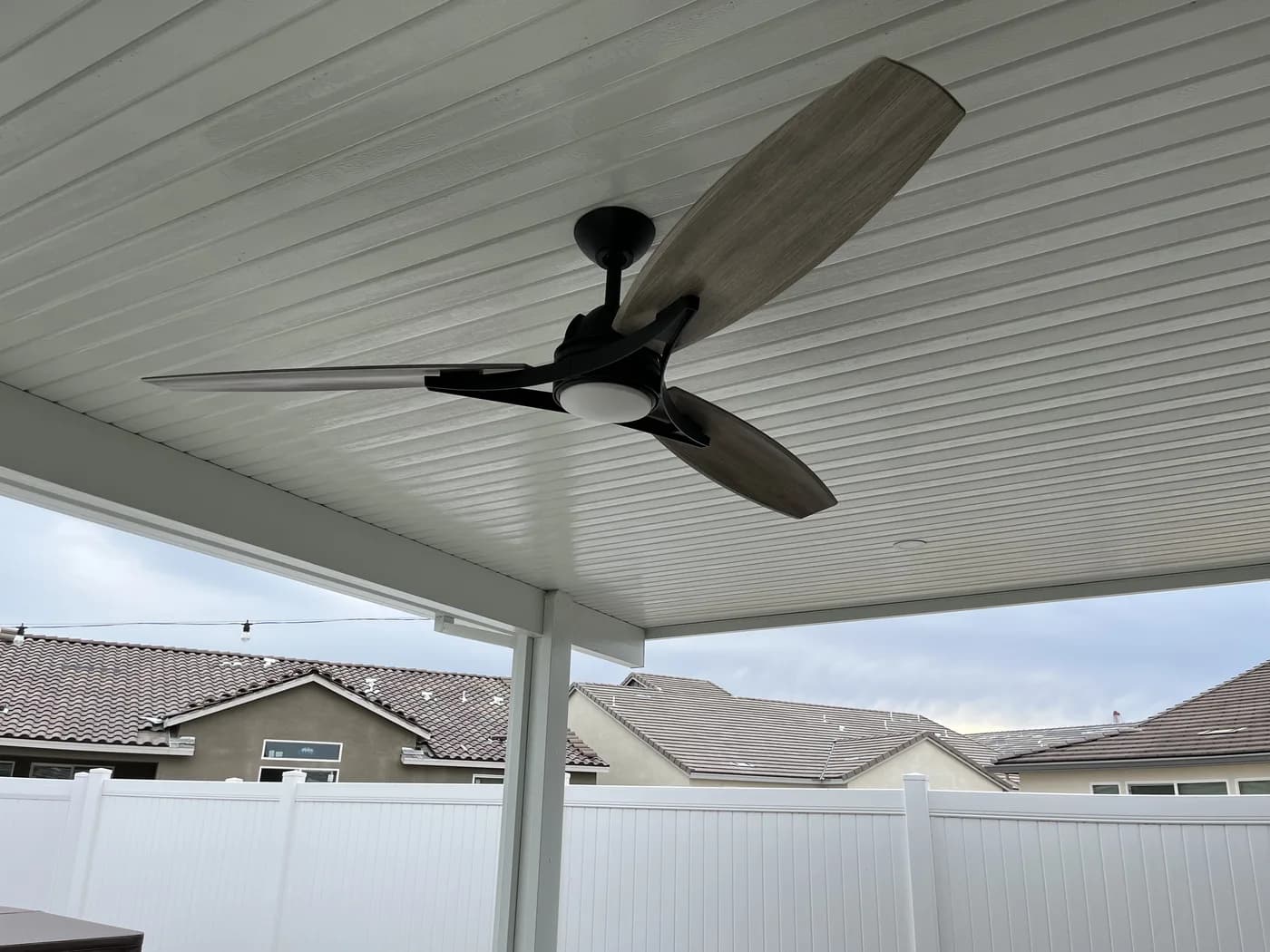 Ceiling fan with a light mounted under a white solid patio cover
