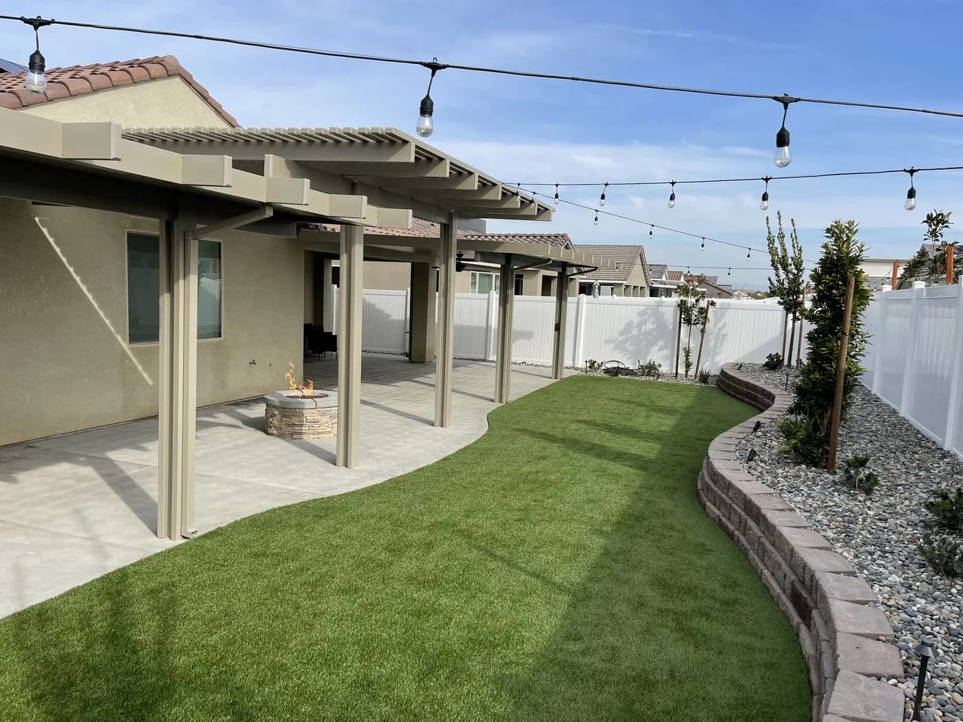 Covered patio with string lights along a turf lawn and a curved block wall