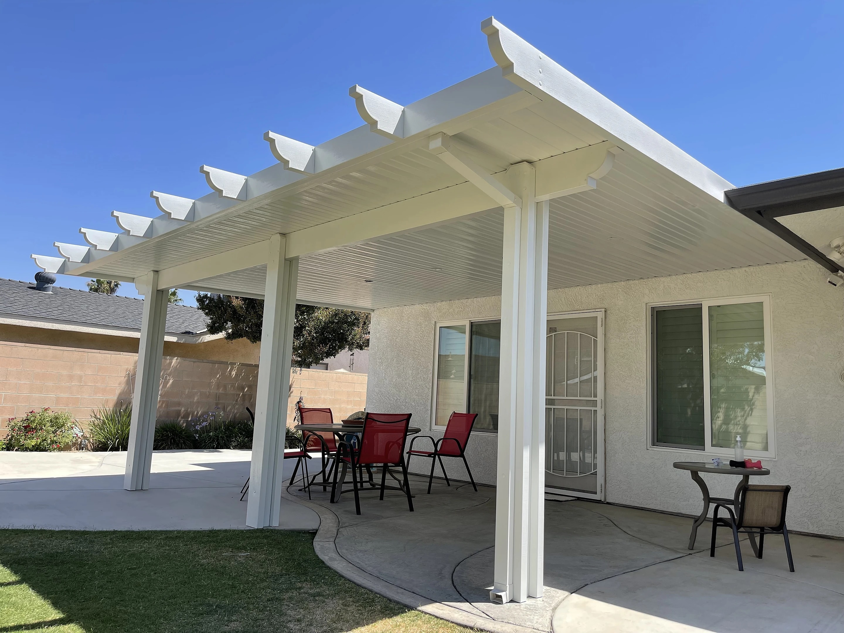 White Alumawood patio cover over a concrete patio with a table and red chairs