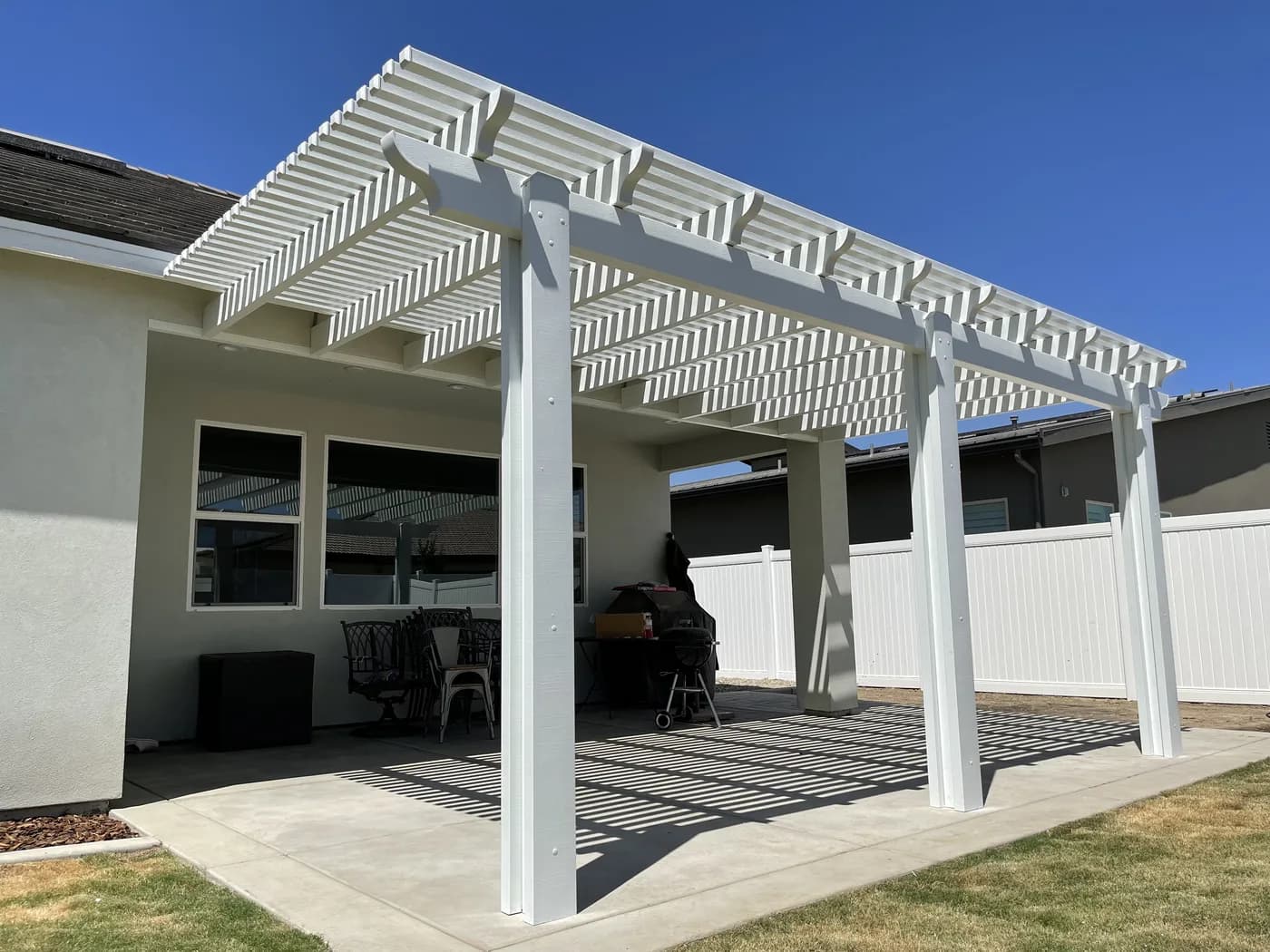White lattice patio cover over a concrete patio with a table and a grill