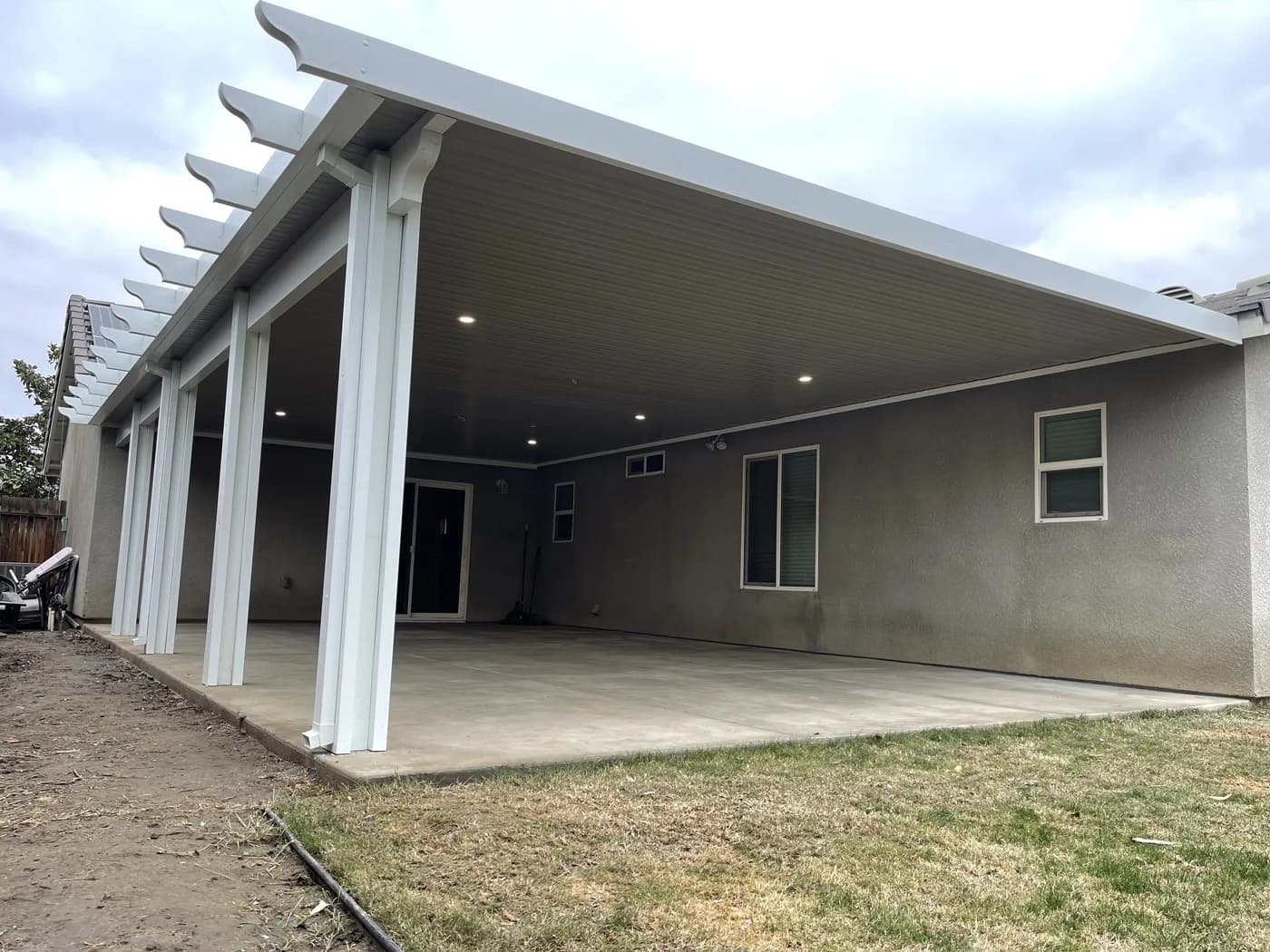 White solid patio cover with recessed lights running the length of a house over a concrete patio