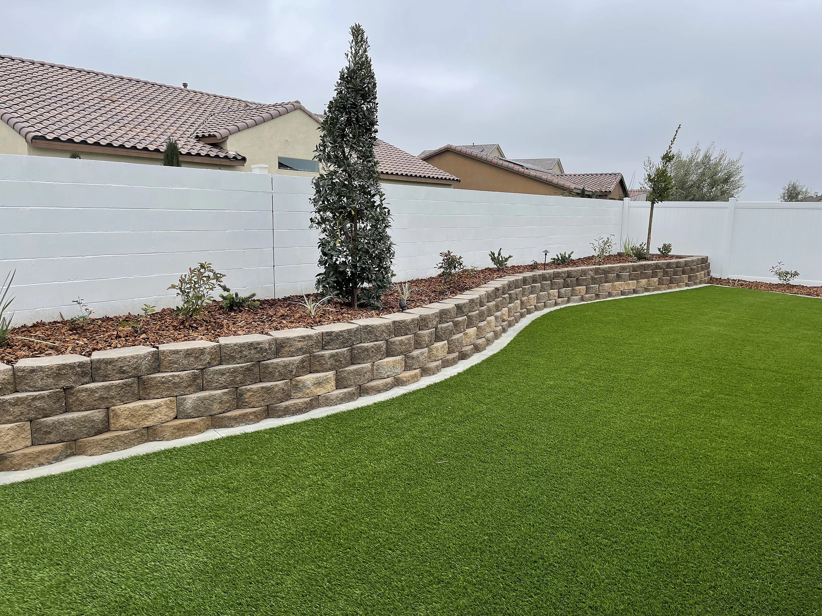 Artificial turf lawn wrapped by a curved block retaining wall and a planted bed